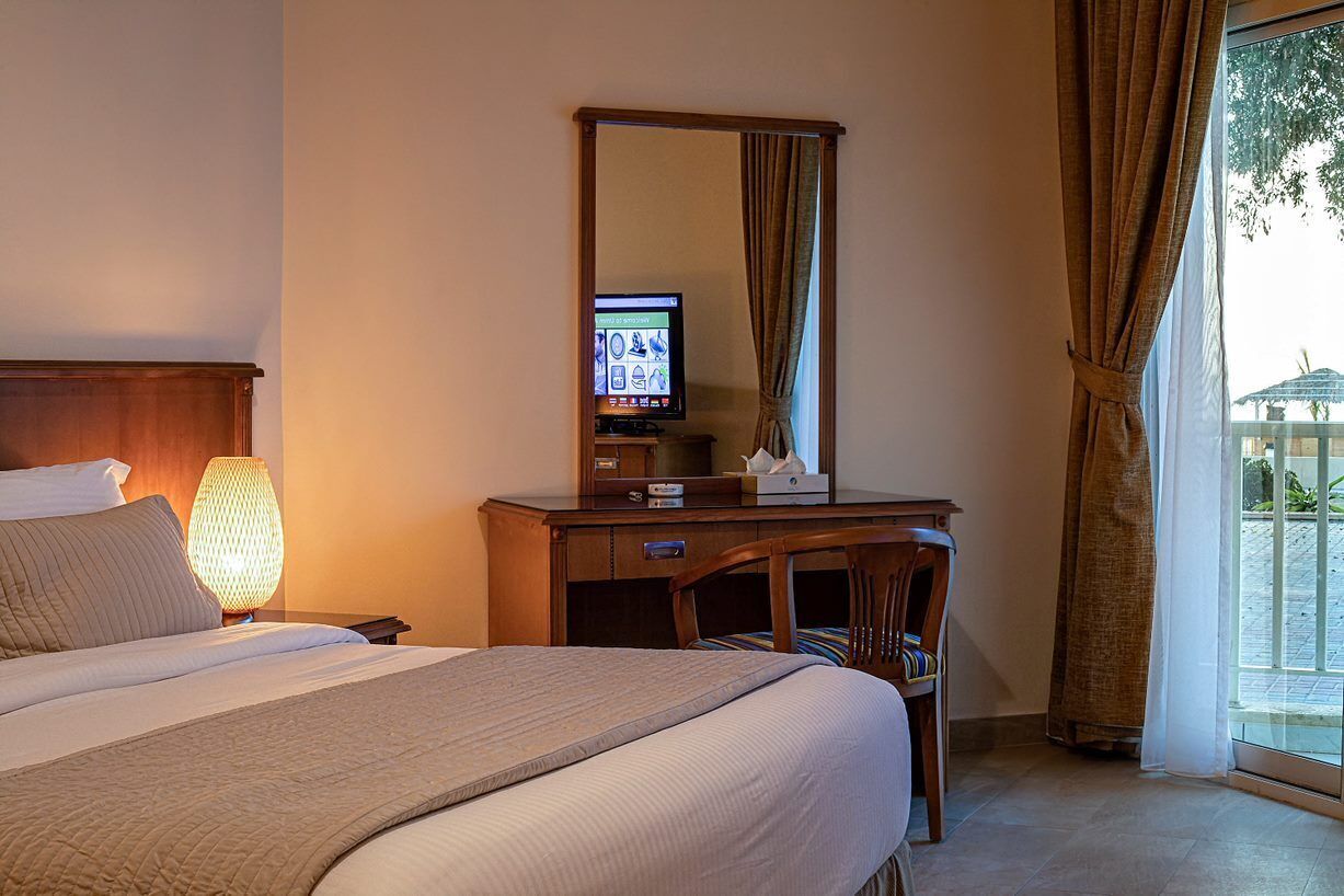 Une chambre d’hôtel avec un lit, un bureau équipé d’un ordinateur, une lampe et une fenêtre avec des rideaux.