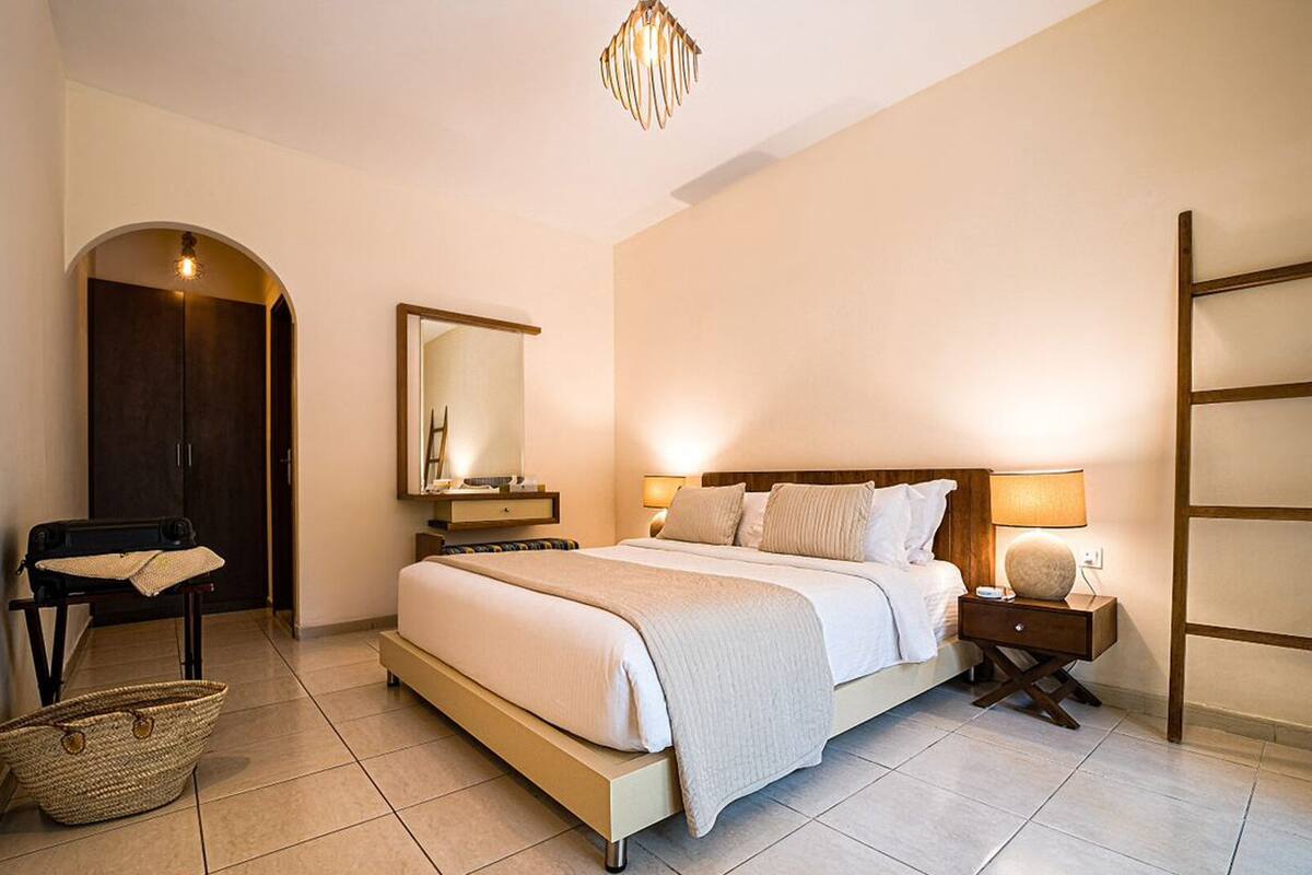 Una habitación de hotel con cama, mesita de noche, lámpara, armario y espejo.
