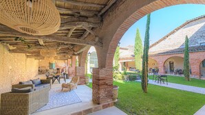 An outdoor patio with wicker furniture, a stone floor, and a brick building in the background. - Le Domaine de la Monestarié<br>Charm, elegance and scents of Tuscany (BERNAC)