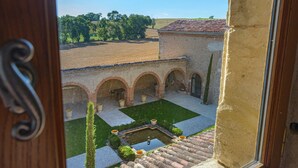 A courtyard with a fountain, arched walkways, and a view of the surrounding landscape. - Le Domaine de la Monestarié<br>Charm, elegance and scents of Tuscany (BERNAC)