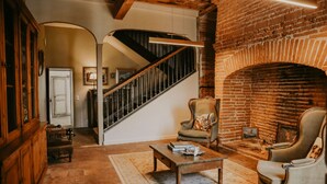 A cozy living room with a brick fireplace, a staircase, and a comfortable armchair. - Le Domaine de la Monestarié<br>Charm, elegance and scents of Tuscany (BERNAC)