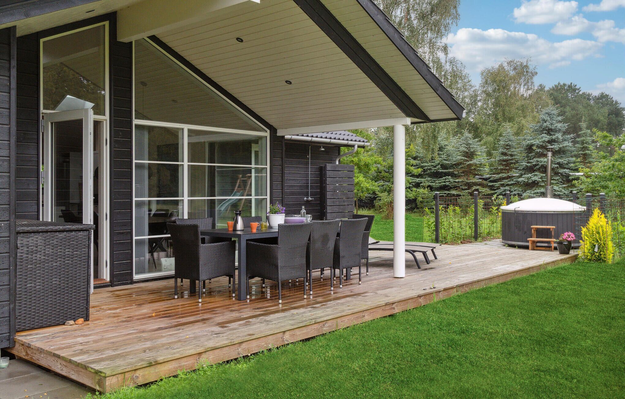 Eine moderne Terrasse im Freien mit Holzboden, einem Esstisch mit Stühlen und einem Whirlpool.