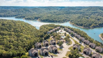Vue aérienne d’un quartier résidentiel avec de nombreuses maisons à deux étages, une route sinueuse et un lac entouré d’une forêt dense.