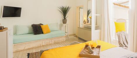 A hotel room with a bed, a sofa, a small table with a tray, a potted plant, and a mirror.