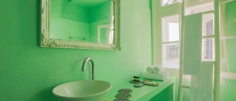 Un baño con pared verde, un lavamanos blanco, un espejo y una ventana con vistas al exterior.