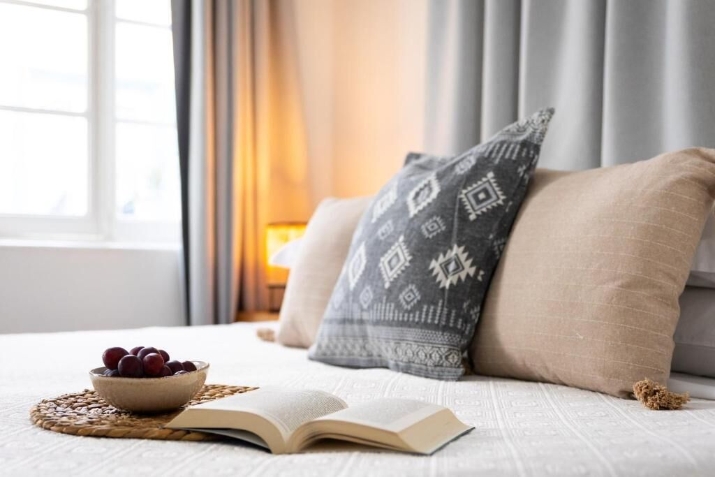 A bed with a book and a bowl of fruit on a woven placemat.