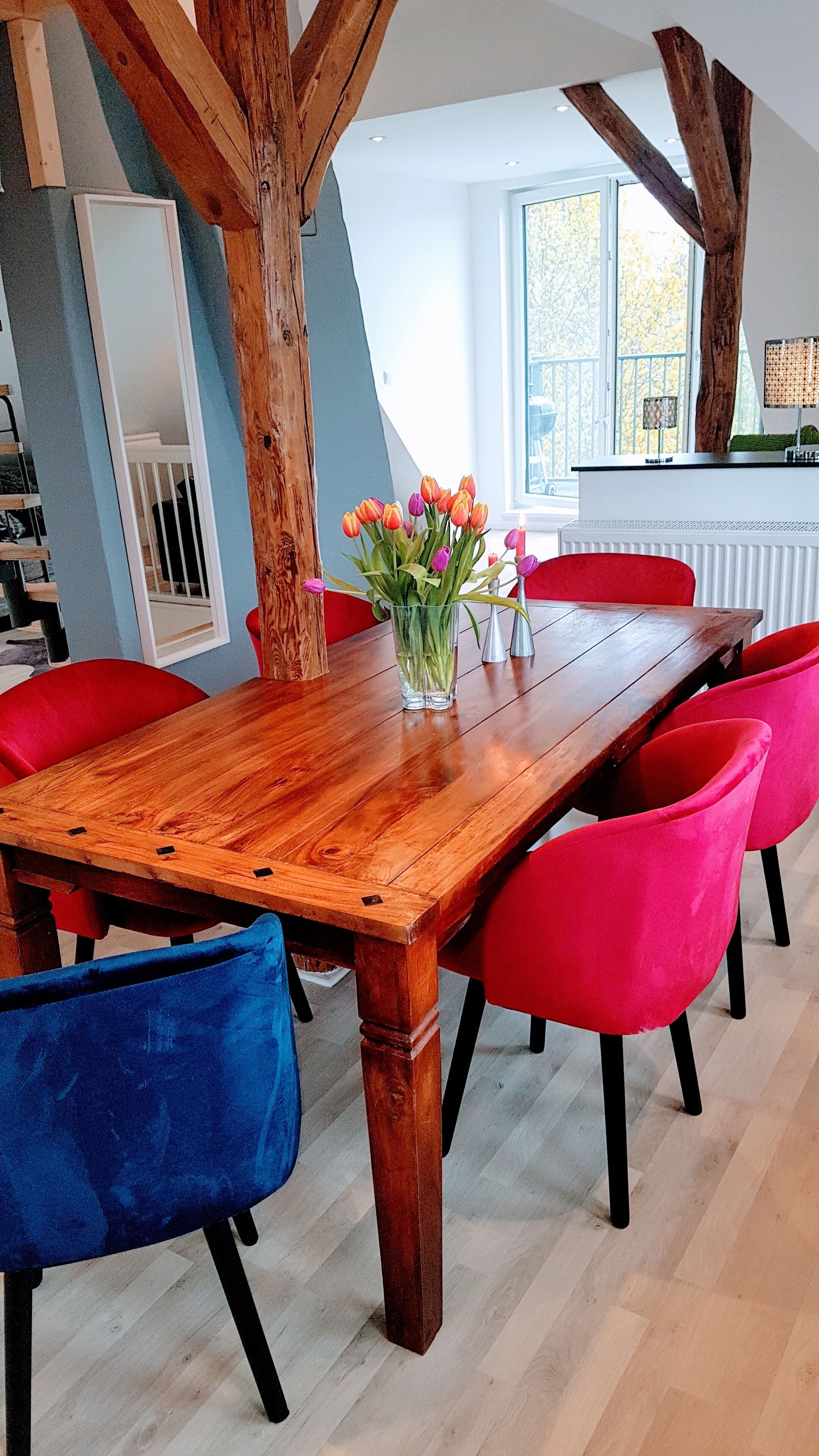 Zona pranzo con tavolo in legno, sedie rosse e un vaso di fiori.