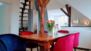 Un coin repas avec une table en bois, des chaises rouges et bleues, un vase avec des fleurs et une vue sur l’extérieur.