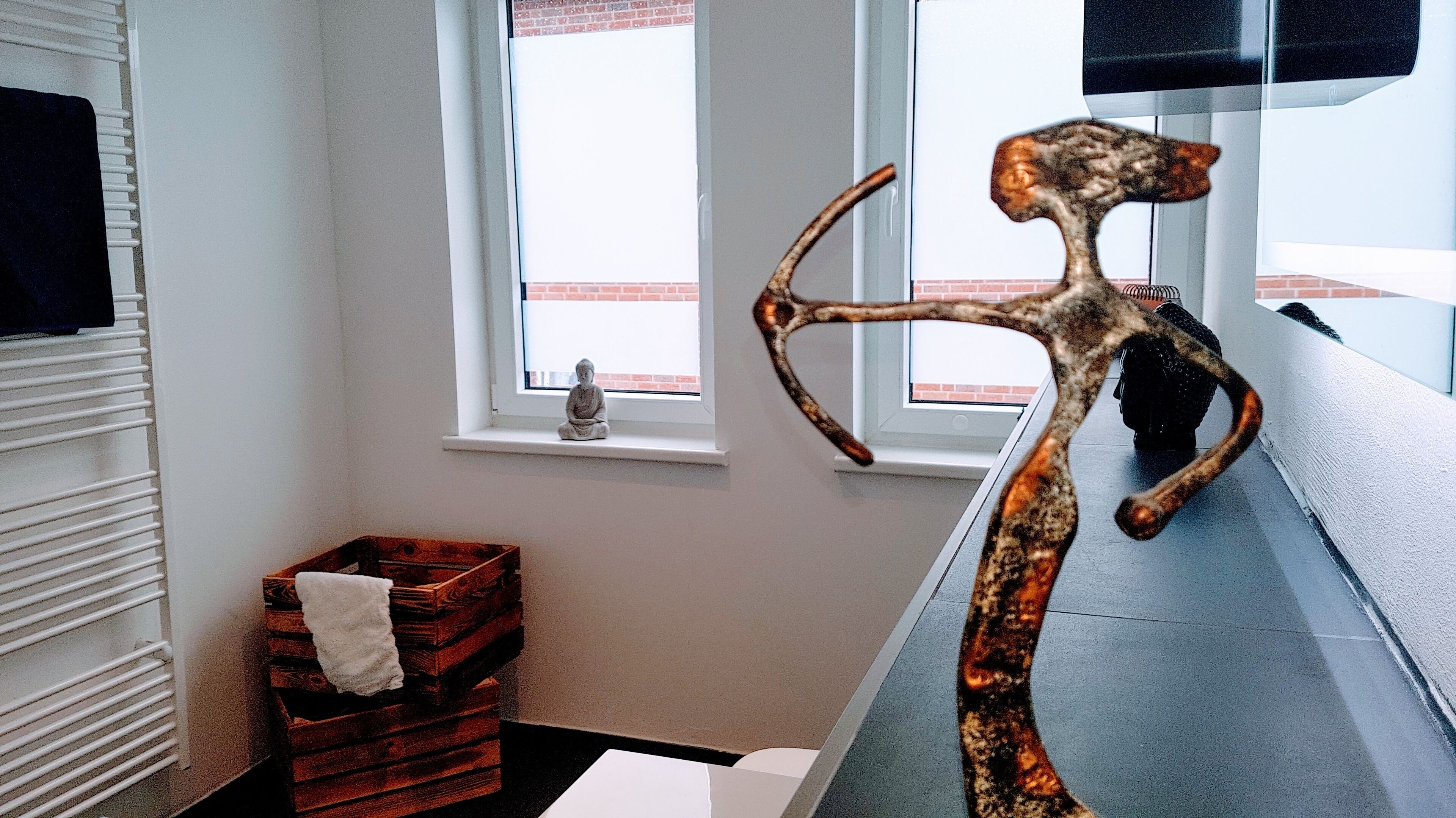 Ein Zimmer mit Fenster, Heizkörper, einer kleinen Holzkiste und einer einzigartigen Skulptur.
