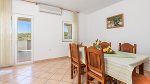Un'area pranzo con un tavolo imbandito per quattro persone, sedie di legno, una tovaglia a righe verdi e una ciotola di frutta sul tavolo.