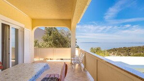 Un balcone con tavolo e sedie, affacciato su un panorama suggestivo di mare e colline.