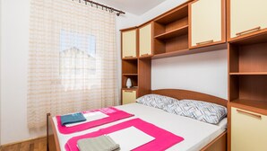 Un letto rifatto con lenzuola rosa e bianche, una testiera in legno e un comodino con una lampada.