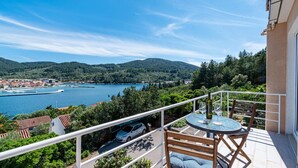 A balcony with a table and chairs overlooking a lake, surrounded by greenery and buildings. - 2 bedroom cozy apartment in Vela Luka (Vela Luka)