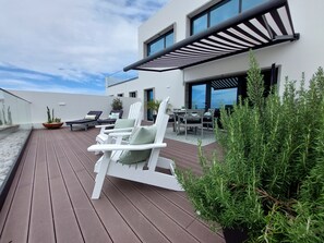Une terrasse extérieure moderne avec des chaises longues blanches, une table à manger et des plantes en pot.