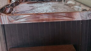 A hot tub with a wooden bench in front, a ceiling fan, and a view of trees through a window. - Twin Oaks: Close to Town! Mtn Views! Hot Tub!  (Bryson City)