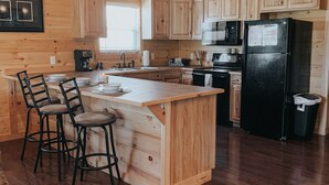 A wooden cabin-style kitchen with a central island, bar stools, a refrigerator, and a microwave. - Twin Oaks: Close to Town! Mtn Views! Hot Tub!  (Bryson City)