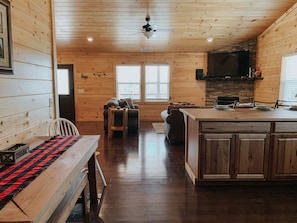 Cozy cabin-style room with a dining table, sofa, and kitchen area.