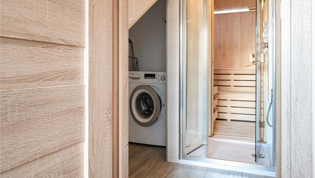 A laundry room with a washing machine and dryer, wooden flooring, and a glass door leading to a sauna area. - 2 bedroom amazing home in Ploskinia (Ploskinia)