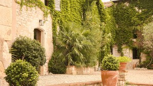 A courtyard with stone walls, potted plants, and a building with ivy. - Le Domaine de la Monestarié<br>Charm, elegance and scents of Tuscany (BERNAC, TARN)