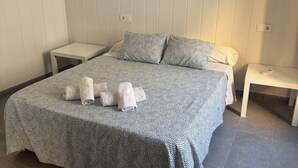 Ein ordentlich gemachtes Bett mit einem gemusterten Überwurf und Kissen, ein kleiner Nachttisch mit einer Lampe und ein gerahmtes Kunstwerk an der Wand.