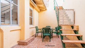 Eine kleine Terrasse im Freien mit einem gemusterten Fliesenboden, einem Tisch mit Stühlen und einer Treppe mit Metallgeländer.