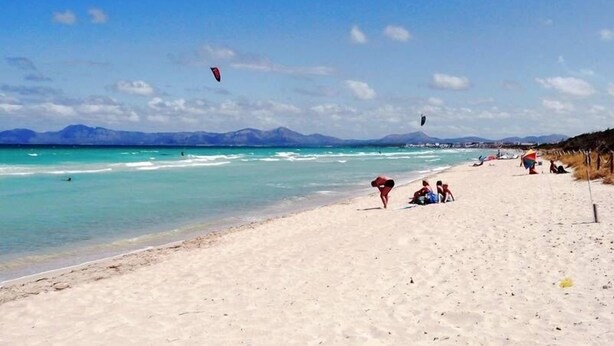 Ein Strand mit klarem türkisblauem Wasser, sandigem Ufer und einigen entspannten Personen.