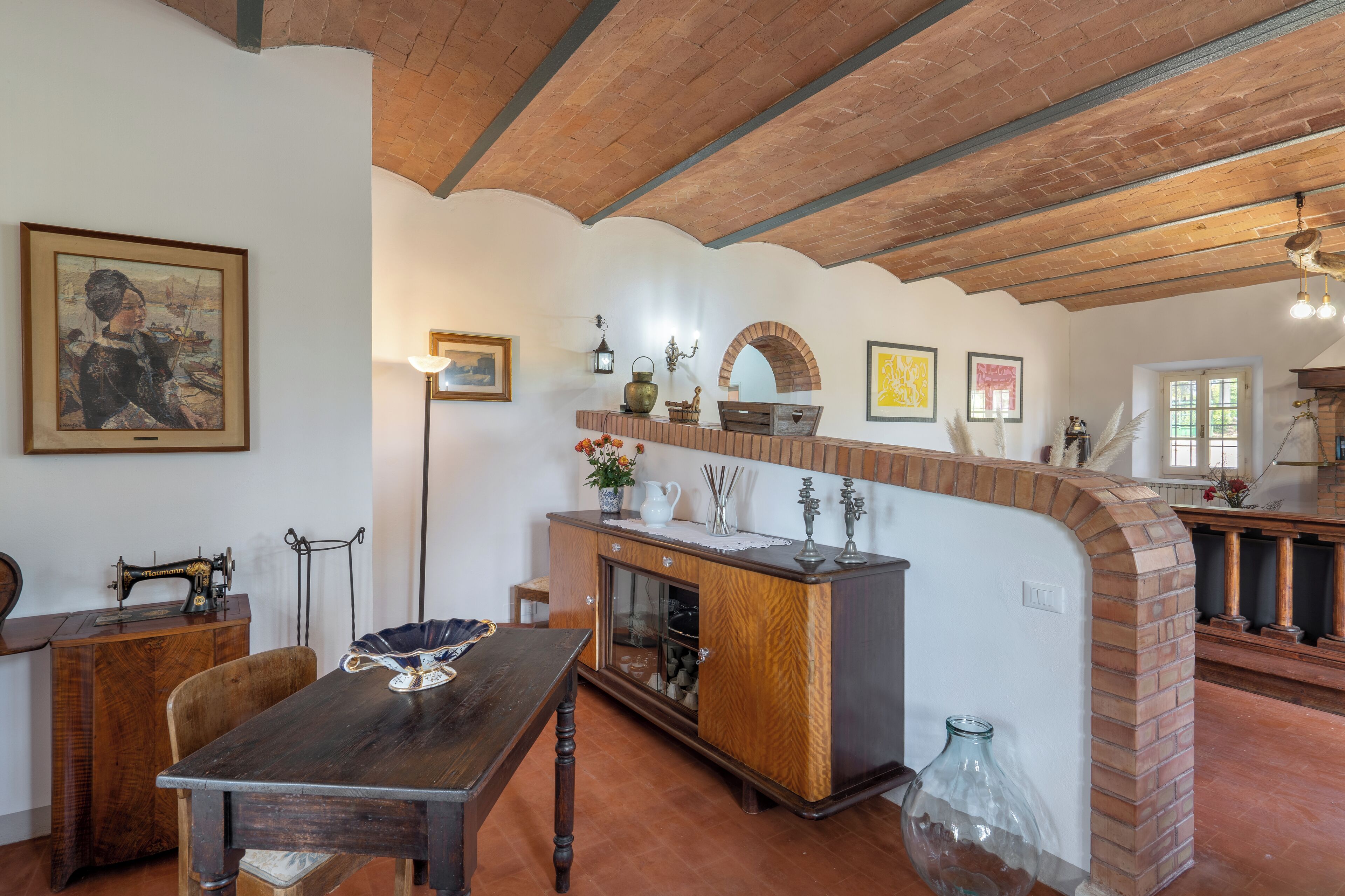 A rustic interior with exposed wooden beams, a wooden table, a cabinet with glass doors, and a brick fireplace.