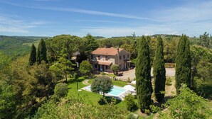 Un'ampia casa con piscina, circondata da alberi alti e un paesaggio collinare.