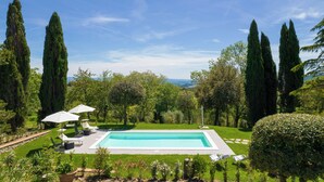 Una piscina circondata da alberi alti e vegetazione, con lettini e ombrelloni.