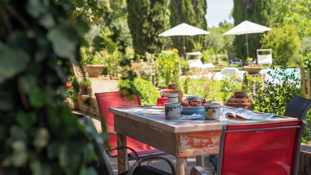 Zona pranzo all'aperto con tavolo apparecchiato per due, immersa nel verde e alberi alti.