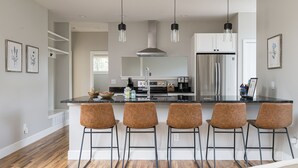 A modern kitchen with a central island, bar stools, stainless steel appliances, and pendant lighting.
