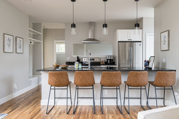 A modern kitchen with a central island, bar stools, stainless steel appliances, and pendant lighting.