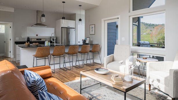 A modern kitchen with a central island, bar stools, and a dining area with a white sofa and coffee table.