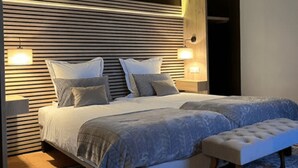 A modern bedroom with a slatted headboard, two bedside lamps, a large bed with a patterned duvet, and a bench at the foot of the bed.