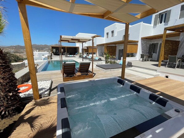 Un espace piscine aménagé sur le toit, comprenant un jacuzzi, des chaises longues et une structure en forme de pergola.