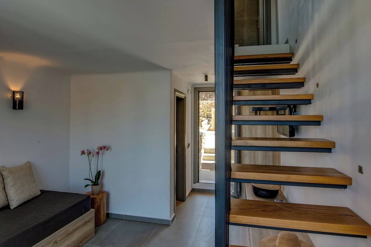 A modern interior with a staircase, a seating area with a cushion, and a wall-mounted light fixture.