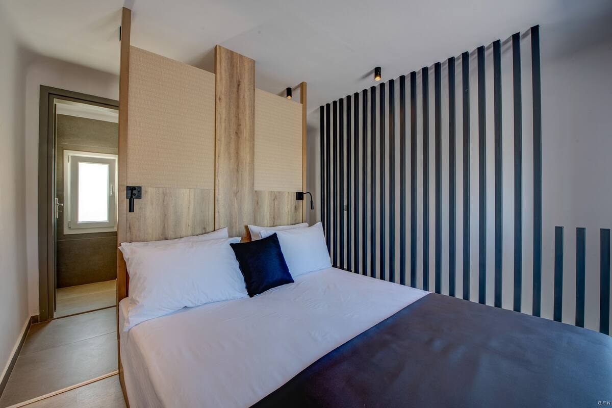 A modern bedroom with a large bed, wooden headboard, and a vertical striped wall design.