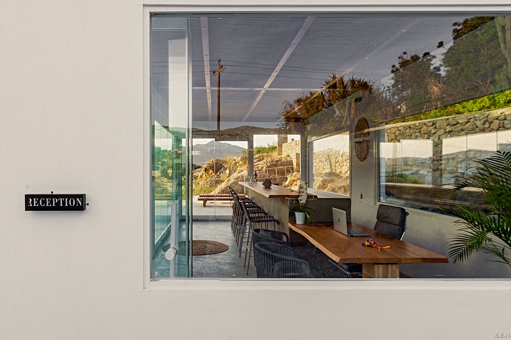 Un área de recepción con pared de vidrio, un mostrador de recepción y una zona de estar con sillas y una mesa.