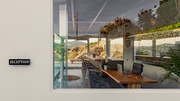 Un área de recepción con pared de vidrio, un mostrador de recepción y una zona de estar con sillas y una mesa.