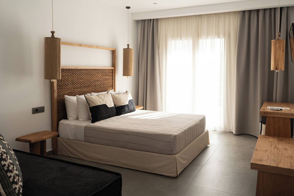 A modern bedroom with a large bed, wooden headboard, bedside tables, and a desk with a chair.