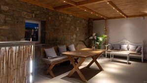 A cozy room with a stone wall, wooden ceiling beams, a wooden table, a bench, and a white sofa.