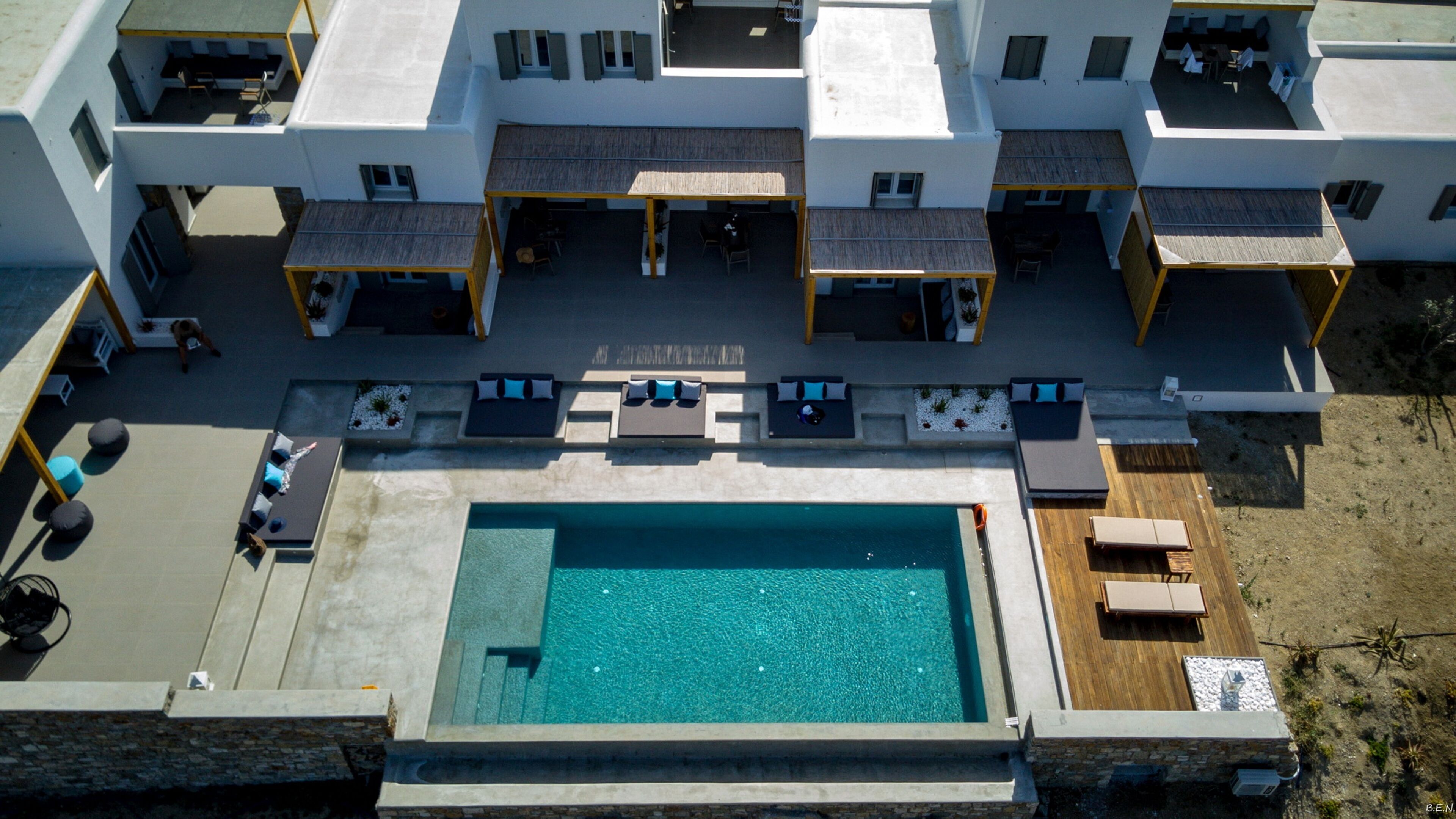 Ein Luftbild eines modernen Hotels mit einem zentral gelegenen Schwimmbad, Außenbereichen zum Sitzen und zahlreichen Balkonen.