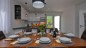 A modern dining room with a wooden table set for six, surrounded by dark chairs. A kitchen with white cabinets and a black countertop is visible in the background. - Lovely home in Zagvozd (Zagvozd)