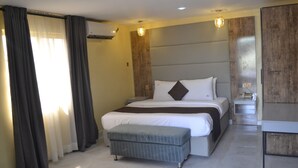 A modern hotel room with a large bed, a bedside table, a small bench, and a wooden accent wall. - Valley Front View Hotel (Lagos)
