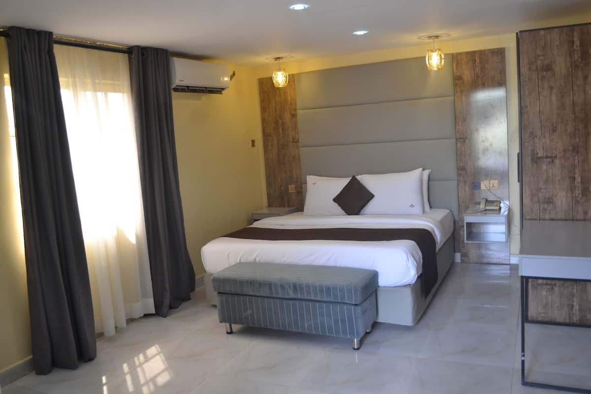 A modern hotel room with a large bed, a bedside table, a small bench, and a wooden accent wall.