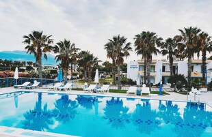 Una piscina con sillas de descanso y palmeras, rodeada por un edificio que dice 'Apartments Olympia'.