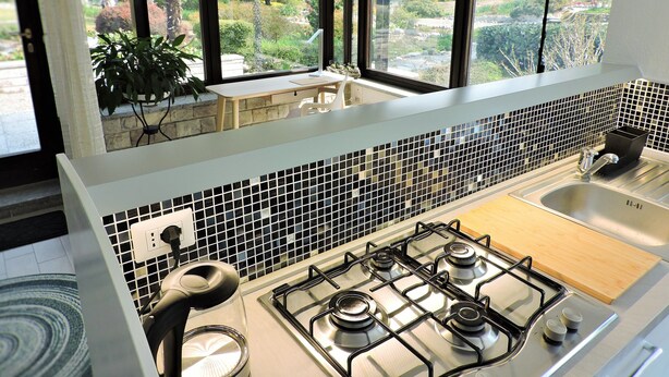 A modern kitchen with a gas stove, a sink, and a view of a garden through large windows. - Spending a vacation in the Garden. (Barzola)