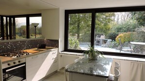 A modern kitchen with a gas stove, white cabinets, and a large window overlooking a garden. - Spending a vacation in the Garden. (Barzola)