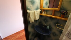 Un baño con un lavabo azul oscuro, un perchero blanco y un estante de madera con artículos de aseo.