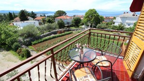 Un balcón con mesa y sillas, con vistas a un jardín y una vista de casas y montañas.
